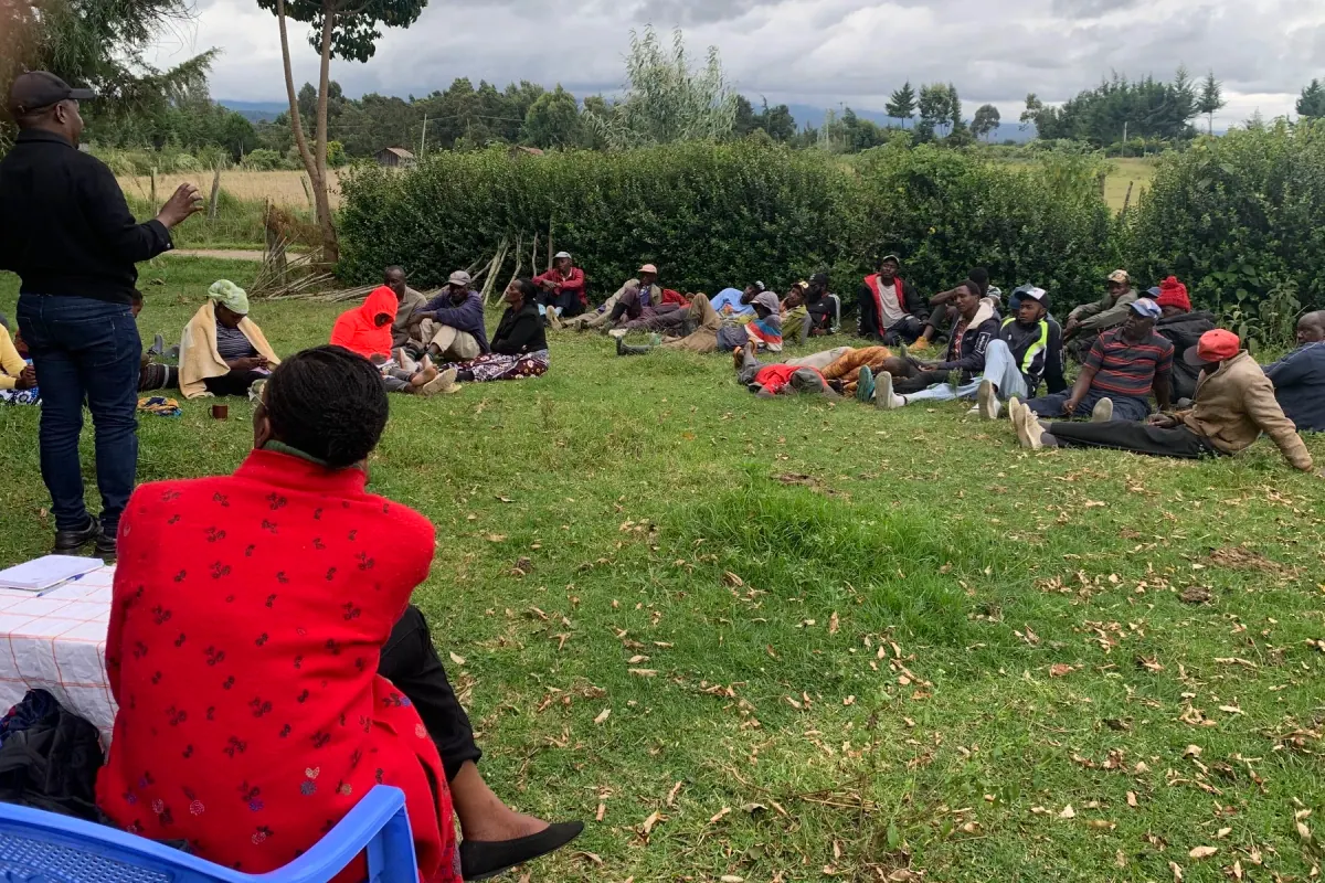A Moedim leader in a red coat watching a farmer meeting in the Mt Kenya region